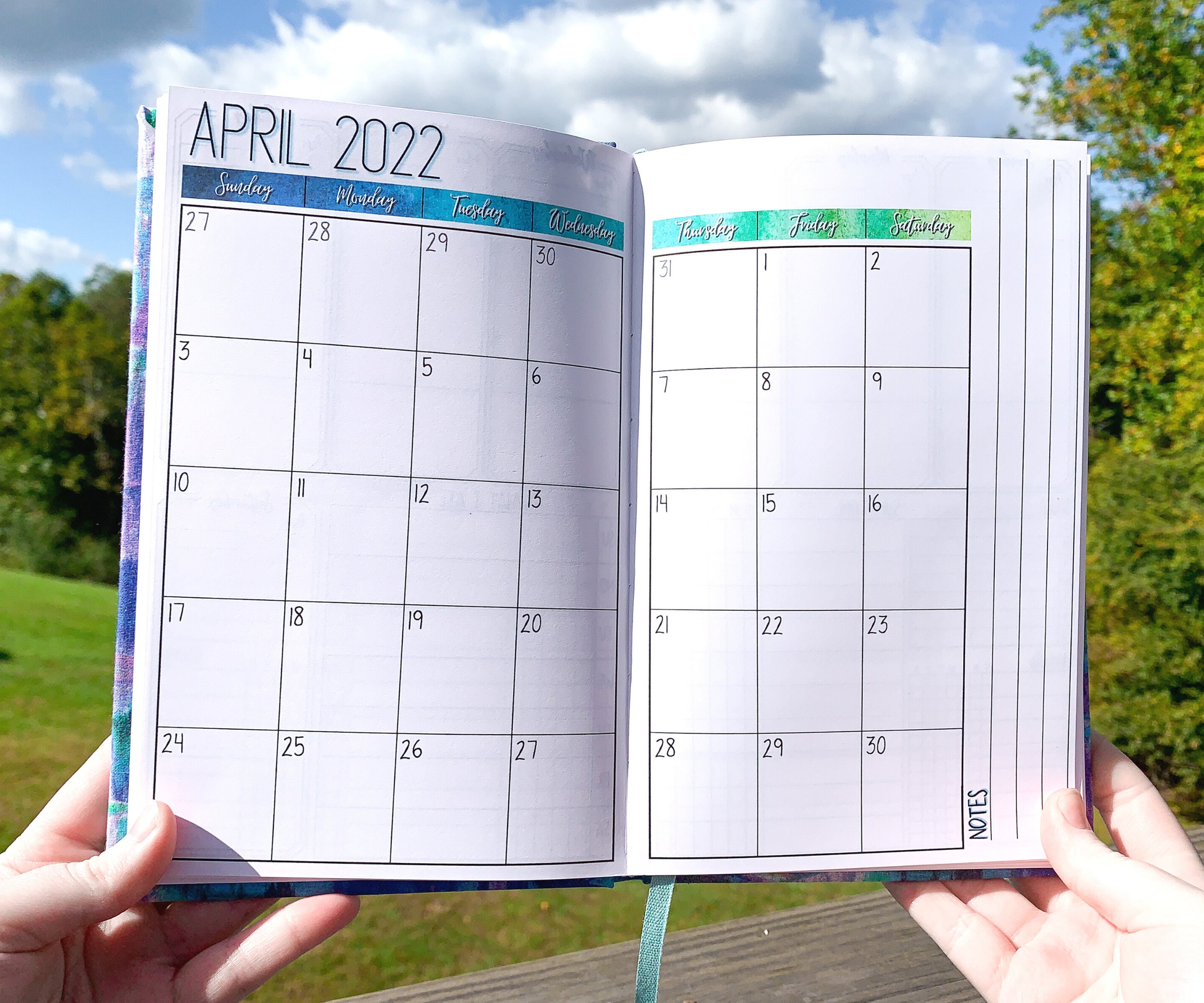 The monthly page is shown. This a calendar page with the month name and year at the top right and a notes writing area on the right side of the calendar box. There is a blue gradient from dark blue to aqua to green where the days of the week are- this is for the blue color journal
