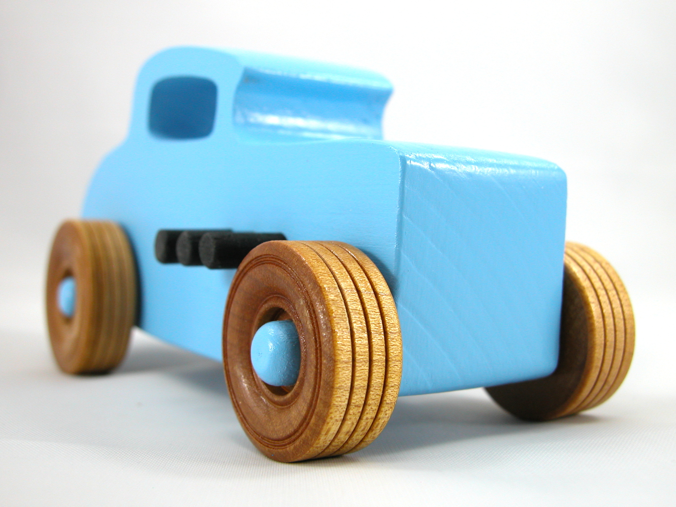 A wooden handmade hot rod toy car modeled after a 32 Deuce Coupe, painted in baby blue and black acrylic paint, with non-marring Amber Shellac wheels.