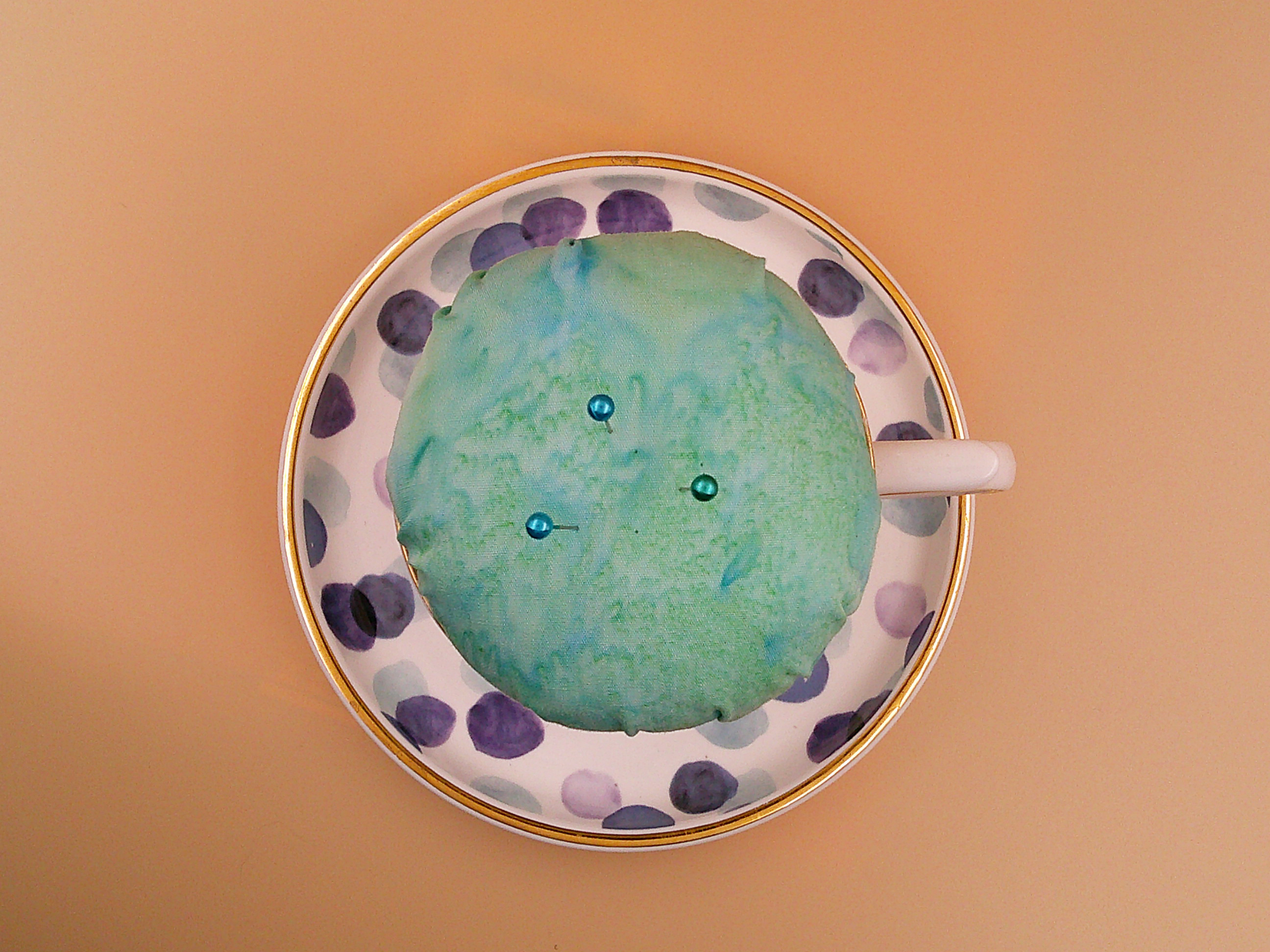 This is a view looking from the top to the bottom of the teacup pincushion/bobbin holder. You can see the pins and the edge of the saucer. This is a view looking from the top to the bottom of the teacup pincushion/bobbin holder. You can see the pins and the edge of the saucer.