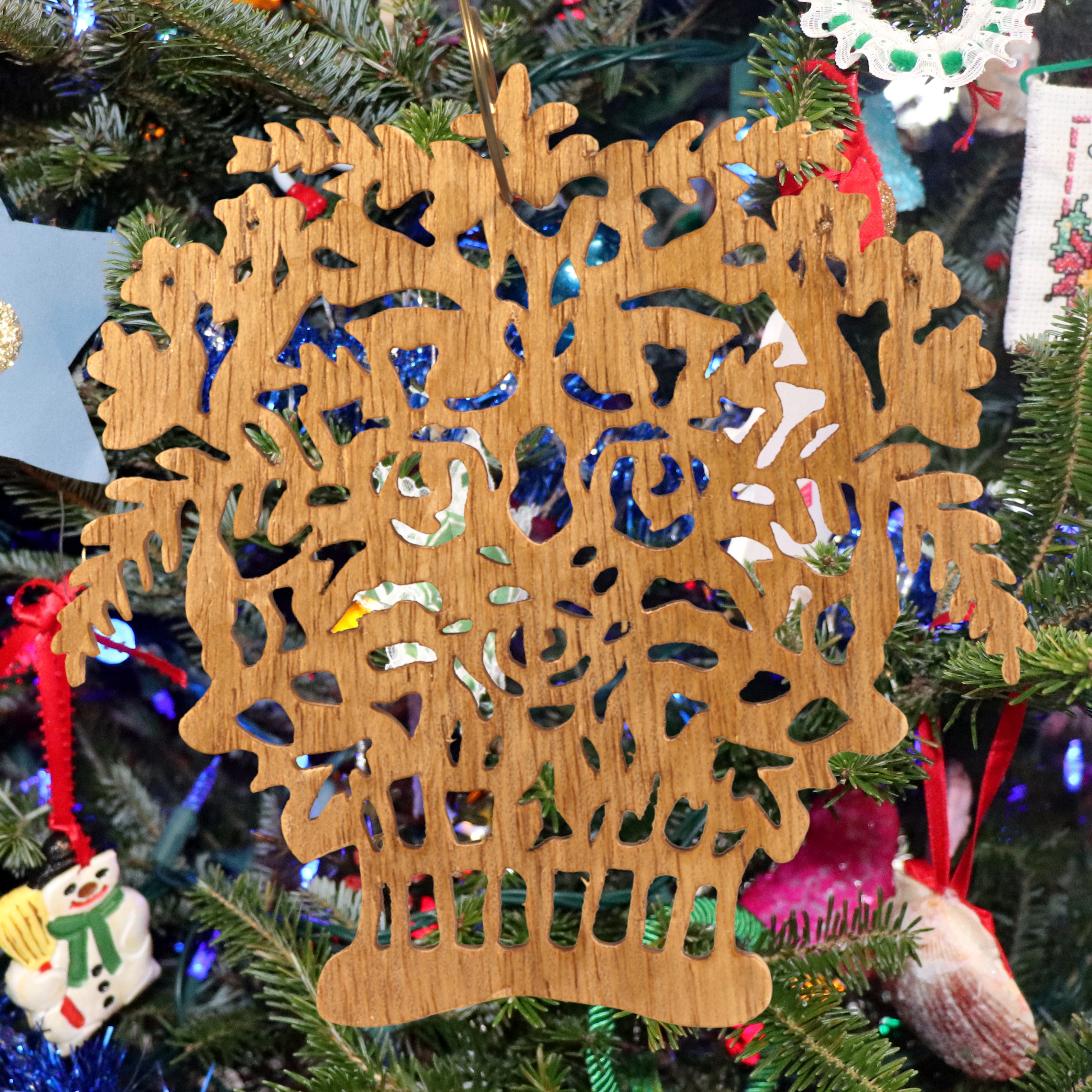 A handcrafted Victorian-style wooden Christmas tree ornament shaped like a basket filled with intricate floral designs, featuring detailed leaves and blossoms, with a small hook at the top for hanging.