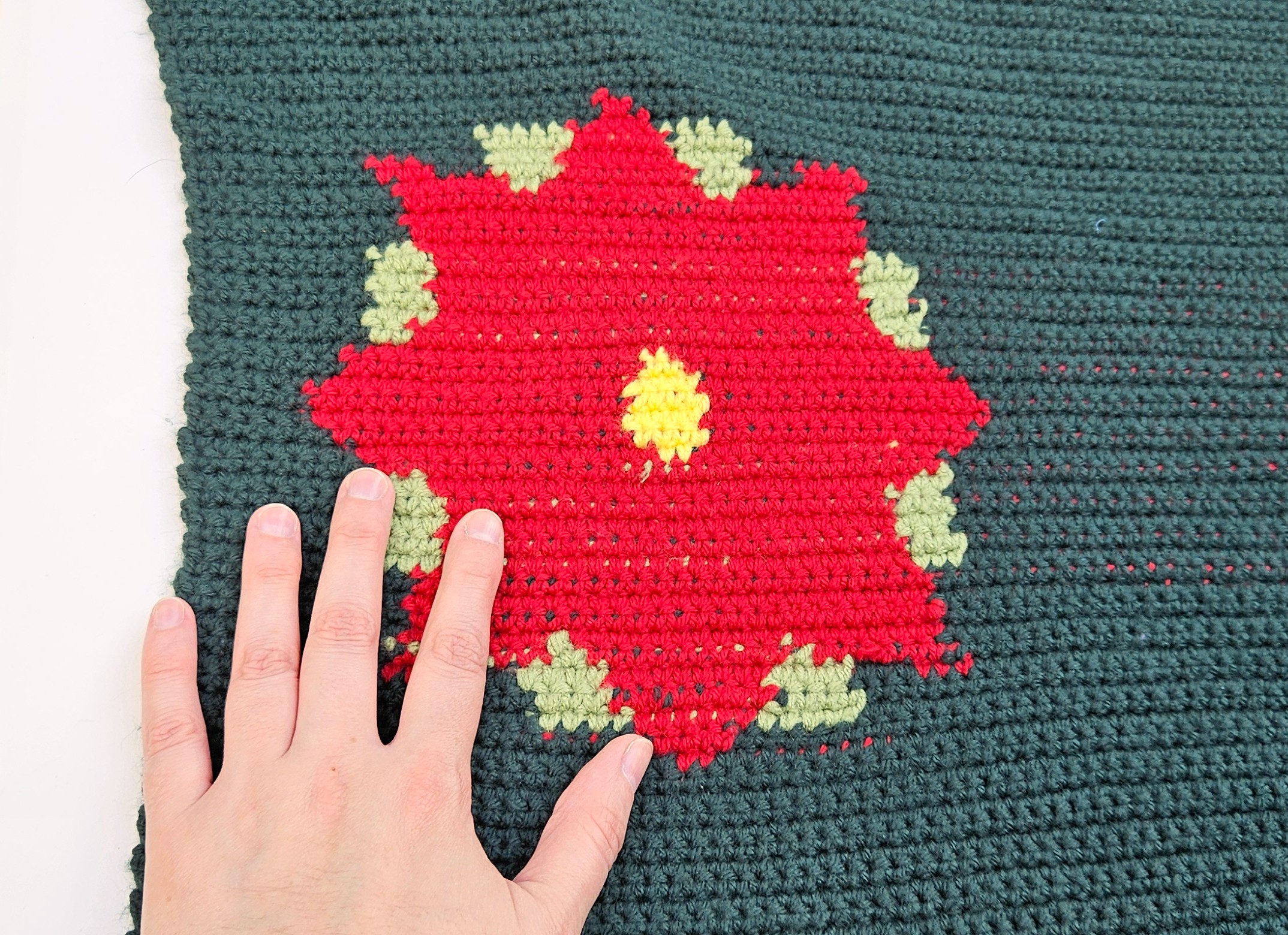 A close up of one of the red poinsettias on either end of the table runner. The maker's hand is in the photo to the left to show size.  A close up of one of the red poinsettias on either end of the table runner. The maker's hand is in the photo to the left to show size.
