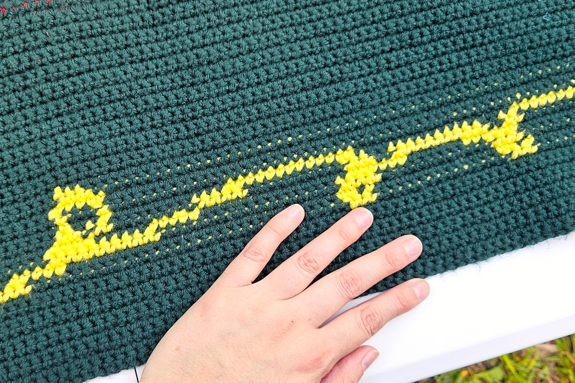 A close up of one of the yellow swirls that appear above and below the quote. The maker's hand is in the photo for size context.  A close up of one of the yellow swirls that appear above and below the quote. The maker's hand is in the photo for size context.