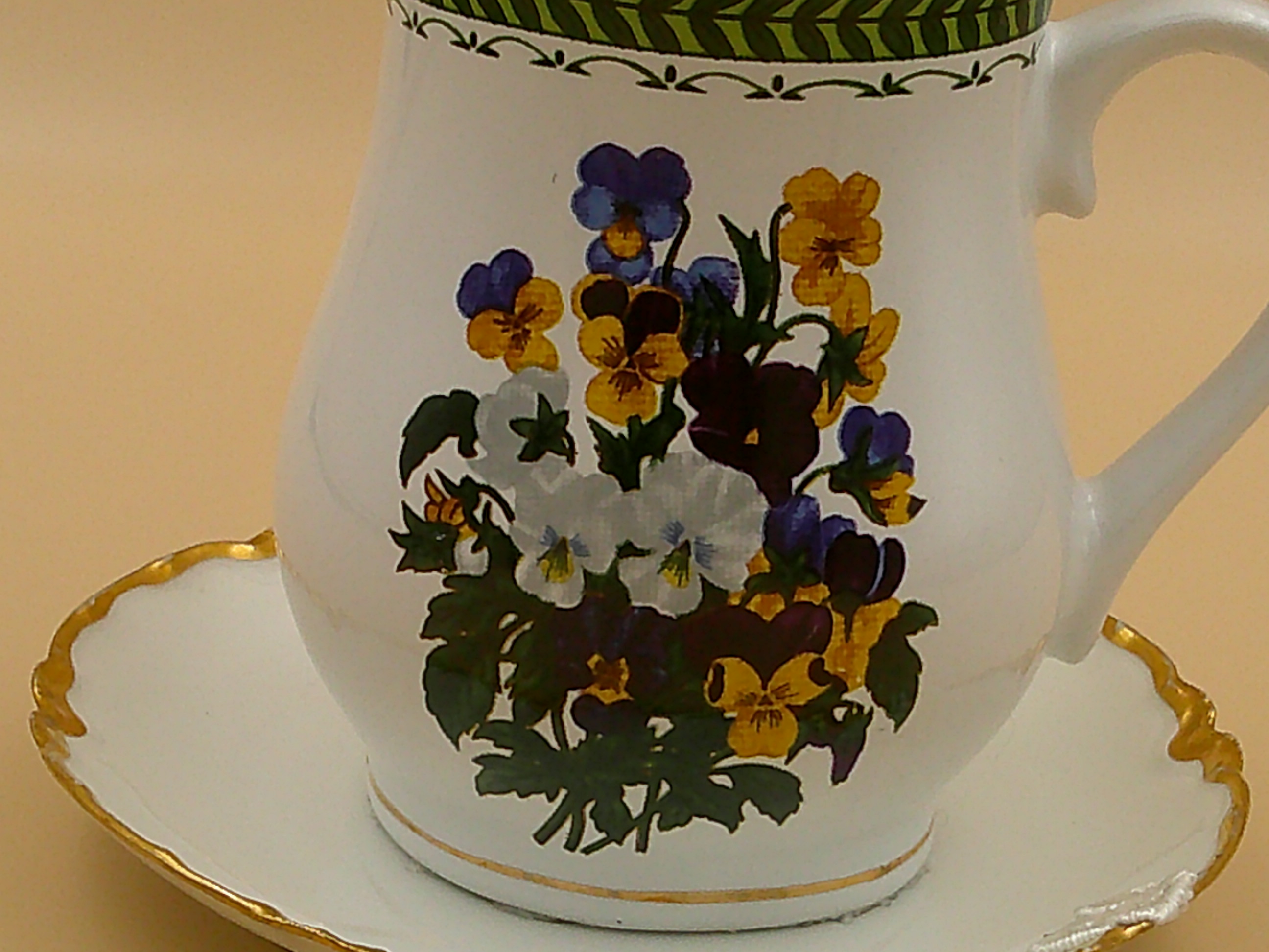 This is a closeup of the vibrant bouquet of pansies. It also shows the gold trim around the base of the cup. This is a closeup of the vibrant bouquet of pansies. It also shows the gold trim around the base of the cup.