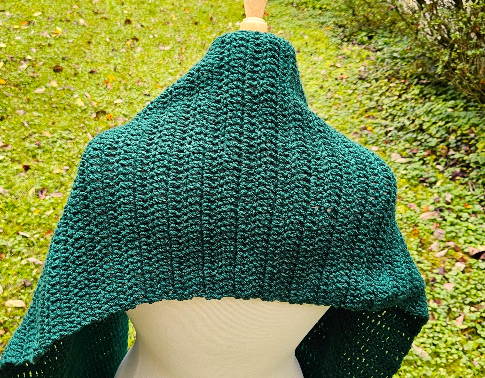A close up of the scarf draped over the shoulders of the dress form. There is green grass in the background. A close up of the scarf draped over the shoulders of the dress form. There is green grass in the background.