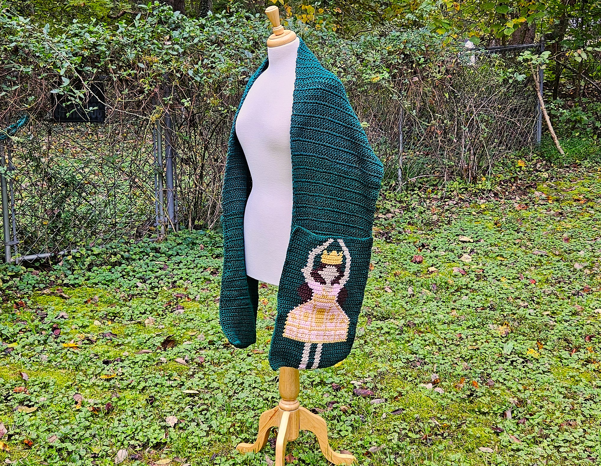 A side shot of the scarf hanging from the white dress form. Tehre is green grass in the background. A side shot of the scarf hanging from the white dress form. Tehre is green grass in the background.