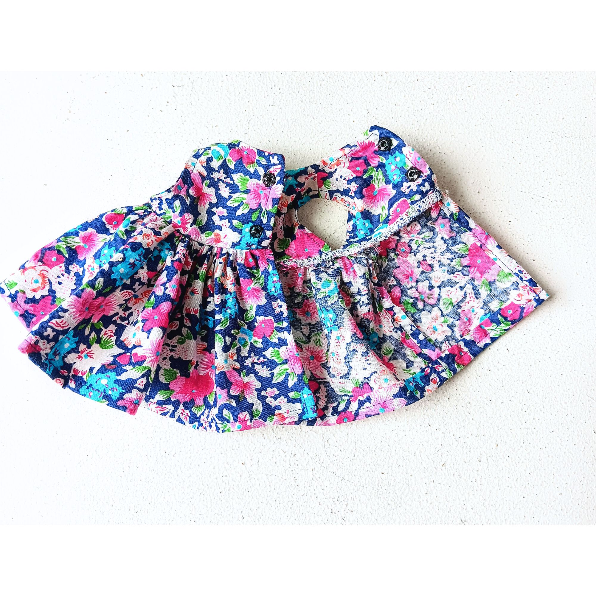 Close-up of the handmade doll’s cotton floral dress, showing delicate gathers and a small back opening. The vintage-style fabric adds color.