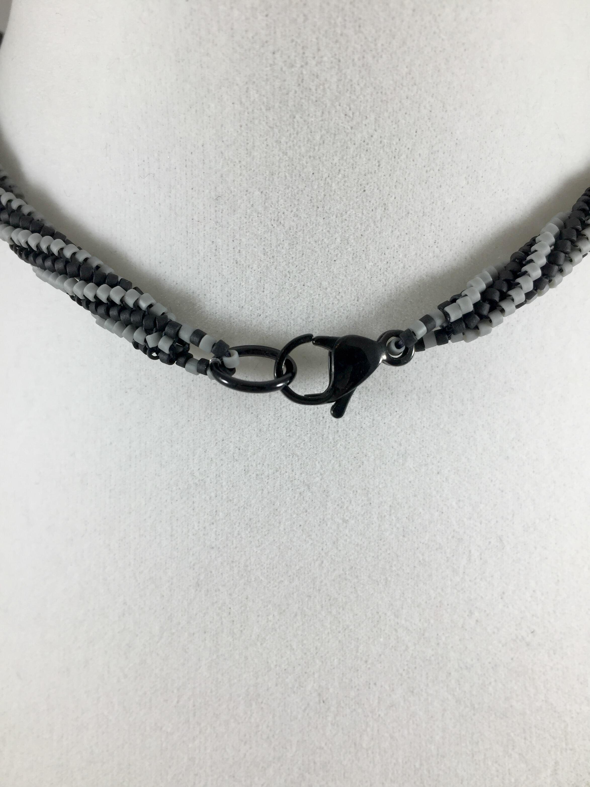 Close up image of black stainless steel lobster claw clasp on black and grey beaded necklace