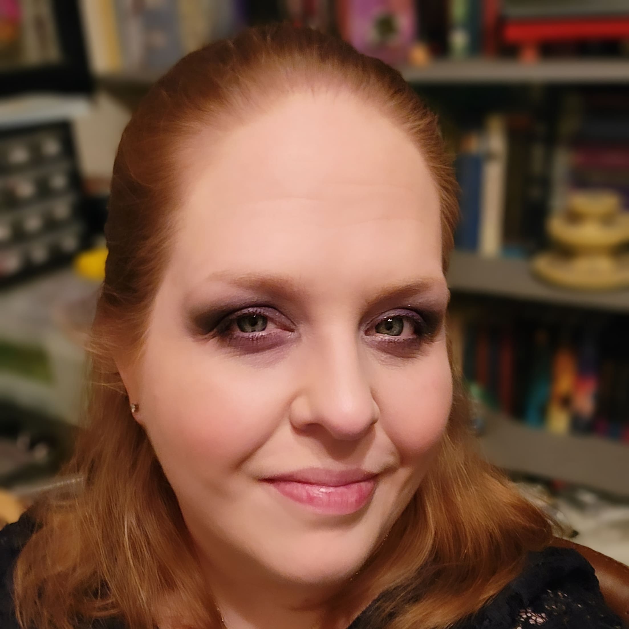 Red head with hair half pulled back smiling in front of bookshelves