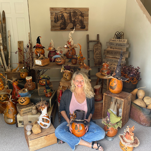 This image shows myself sitting with many decorative gourds I have made. A wood burned bear hangs on the wall that I made.