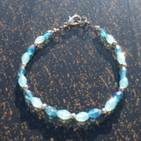 Frozen-theme bracelet rests on a table. There are 3 types of beads: iceberg blue (glass), blizzard blue (glass), & stainless steel (metal).