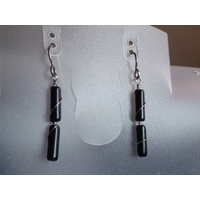 Black obsidian earrings hang on a jewelry stand. There are 2 tube smooth stones on each earring in this photo.  Black obsidian earrings hang on a jewelry stand. There are 2 tube smooth stones on each earring in this photo.