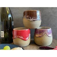 Three ceramic, hand-thrown wine tumblers, red, brown and purple. Each tumbler holds 12 ounces.