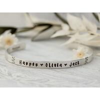 Sterling silver cuff bracelet stamped with kids names and a heart spacer between names with a stamped for detail on both sides.  Sterling silver cuff bracelet stamped with kids names and a heart spacer between names with a stamped for detail on both sides.