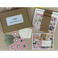 Card making kit with gold foil floral patterned scrapbook paper, pink cardstock, pink flowers, green ribbons and off-white Bloom sentiments.