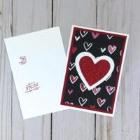 A valentine card making kit of 12 with black scrapbook paper with hearts, white and red heart embellishments, and white cards and envelopes.