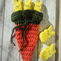 Medium dark orange crochet carrot pouch with dark green top with 3 peep marshmallow bunnies poking out of the top to show width. Medium dark orange crochet carrot pouch with dark green top with 3 peep marshmallow bunnies poking out of the top to show width.