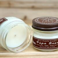 Apple, maple, and cinnamon scented soy candle in 4oz mason jar. One jar standing up with lid on and one jar on its side with lid off.