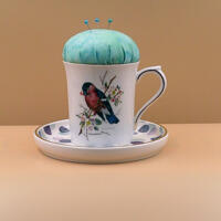 This teacup has a pincushion on the top with some pins and a saucer on the bottom to hold bobbins and other things. It is all one piece. This teacup has a pincushion on the top with some pins and a saucer on the bottom to hold bobbins and other things. It is all one piece.