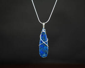 Blue teardrop stone wrapped in a crisscross pattern and swirl at the top with silver wire. It is on a silver chain.