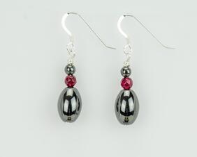 Black oblong earrings accented with dark red faceted beads which are topped by another black bead. The earrings have Silver ear wires