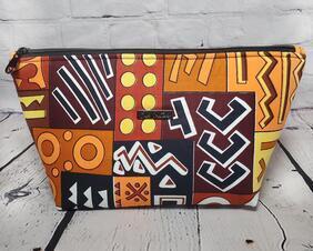 Front of a brown orange and yellow geometric print cosmetic bag with a gunmetal zipper and Bass Creations logo.