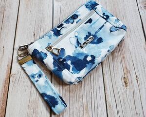 Side view of a blue splotches makeup pouch with two silver zippers and a silver metal Bass Creations logo.