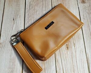 front view of a caramel wristlet with gunmetal hardware and a gunmetal Bass Creations logo.