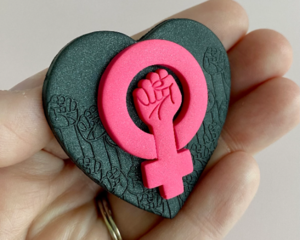 fireflyFrippery hot pink feminist fist on black heart background pin in hand