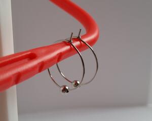 Surgical stainless steel hoops with a bead on each earring hang on a display. Surgical stainless steel is medical grade steel.