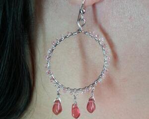 Person models earring. Tiny light pink seed beads wire wrapped on the outer rim of the silver hoop. 