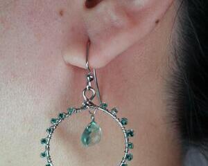 Tiny teal seed beads wire wrapped on the outer rim of the steel gray hoop. A teal teardrop bead hangs from the top center of the hoop. 