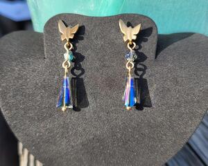 Butterfly post earrings hang on a jewelry display. This photo was taken with the sun shining on them, and the denim beads shine beautifully.