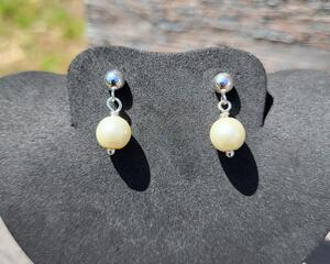 Tiny silver plated pearl post earrings are on a jewelry display. This photo is taken in the sun, so the pearls look whiter than they really are.