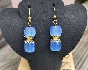 Each earring has two faceted blue beads strung vertically with two intricately detailed gold bead caps in between.