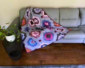 Handmade throw quilt, 54 X 63, in bold colors of bright pink, magenta, royal blue, burnt orange on a background of grayish orchid. Fabrics include striped cats and florals. Backing is a very bright pink with speckles of magenta and gold metallic.
