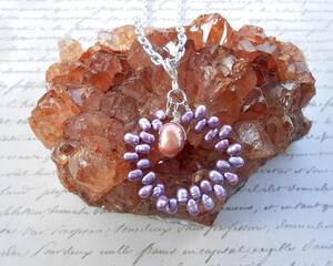 A pendant of purple pearls on a hoop with a larger purple pearl dangling from the top center hanging from a silver chain