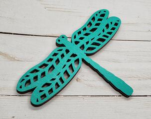 A bright Aqua painted wooden dragonfly on a faux wood background.
