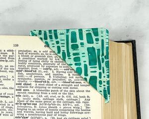 A green batik cotton fabric corner bookmark with a modern pattern.  It's shown on the corner of a page in a book to help mark your spot.
