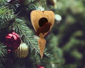 The wooden miniature Birdhouse Ornament is shaped like a heart. A small, dark-reddish-brown bird is perched on the front of the birdhouse. The heart-shaped structure has a pointed bottom that tapers down to a fine point. The wood is light beige.