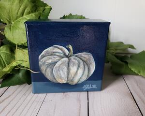 Photo of small square canvas painting of oddly shaped light blue pumpkin with a dark blue background