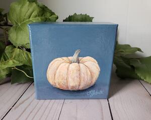 Photo of small square canvas painting of peach colored pumpkin with denim blue colored background