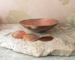 photo showing hand hammered copper trinket bowl 3 inch diameter shown with small oval tokens with "moody" and "neutral" stamped. Third token is left blank.