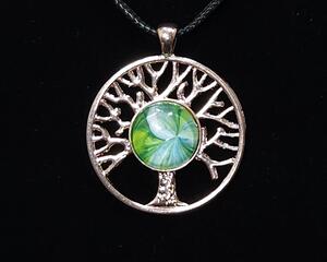 Gold tone tree of life pendant. Green background and white shapes that resemble flower petals.