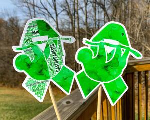 The word cloud and watercolor designs are shown on 2 sticks. Both ribbons feature a green color awareness ribbon with a hanging sloth in the center. The word cloud design on the left is split in half with a word cloud on the left half of the ribbon and right half of the sloth.