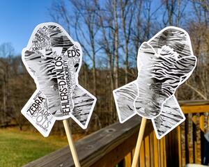 The word cloud and watercolor designs are shown on 2 sticks. Both ribbons are black and grey zebra stripes with a zebra head in the center. The word cloud design on the left is split in half with a word cloud on the left half of the ribbon and right half of the zebra. The right watercolor ribbon is all zebra patterned with a white border around the zebra for definition.