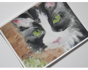 Tuxedo cat watercolor face printed on textured fine art paper. Has large green eyes and pink nose and ears. Stares directly at the viewer. 