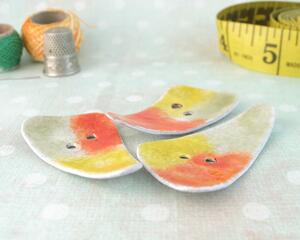 photo showing three abstract triangle copper enamel buttons with yellow, orange, and olive green torch fired enamel on copper. In photo are thread spools and measuring tape for vignette.