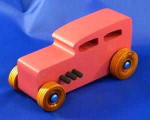 Handcrafted pink wooden hot rod '32 sedan toy car. Features black and metallic sapphire blue accents, and non-marking amber shellac wheels. Made to order for unique play or display.
