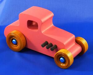 Handmade wooden toy car '27 T-Coupe Hot Rod painted pink with metallic sapphire blue, black trim, and nonmarring amber shellac wheels.