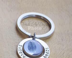 Silver key chain with custom fingerprint charm encircled by hand-stamed Forever in my heart charm on neutral wood background.